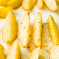 Delicious baked potatoes with rosemary on parchment, closeup. Vegetarian food. Potato country style