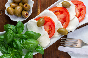 Swieza mozzarella z plastrarmi pomidora i listkami bazyli. Rustykalna kuchnia. Wegetarianskie danie. Vege salatka. © ff25