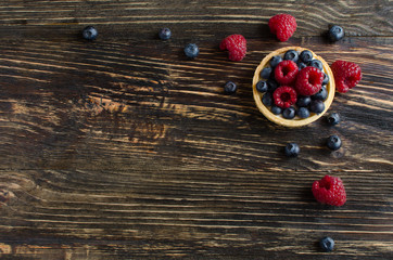 Homemade mini tart with fresh raspberries and blueberries on dark wooden background