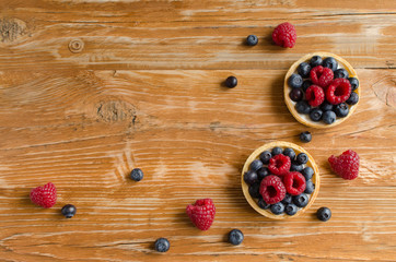 Homemade mini tarts with fresh raspberries and blueberries on wooden background