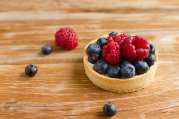 Homemade mini tart with fresh raspberries and blueberries on wooden background