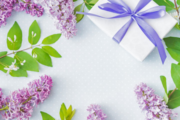 Flat lay composition with branches of lilac and gift box with blue ribbon on a blue background