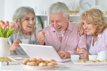 Portrait of happy senior people with laptop drinking tea