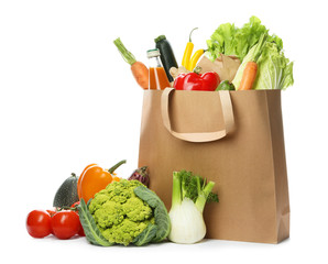 Paper bag with fresh vegetables and bottle of juice on white background