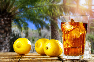 Fresh cold ice tea on desk and blurred background of palms. 