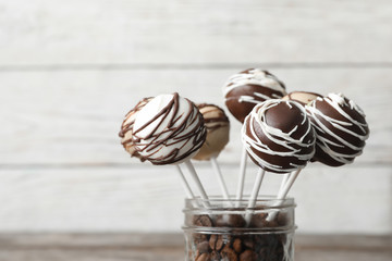 Yummy cake pops coated with chocolate in glass jar full of coffee beans on blurred background, closeup. Space for text