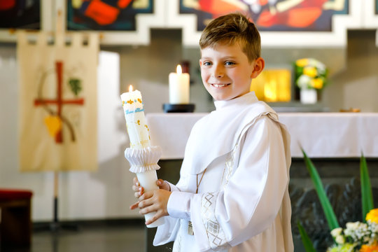 Little kid boy receiving his first holy communion. Happy child holding Christening candle. Tradition in catholic curch. Kid in a white traditional gown in a church near altar.