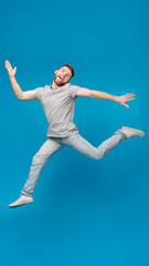 Fototapeta na wymiar Funny millennial guy jumping in air and fooling