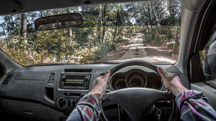 Close up two hands of traveler holding steering wheel driving in the forest road, beautiful nature.
