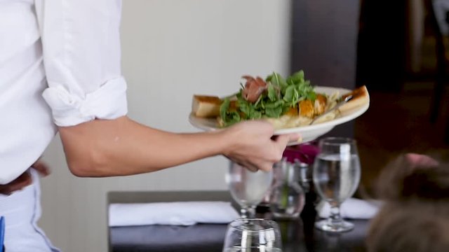 waitress places dinner dishes on restaurant table of young family. A waitress places food dishes in front of husband, wife and young son at a nice restaurant.