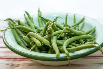 Freshly picked organic green beans in a vintage enamel bowl on a red stripe linen kitchen cloth