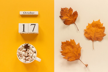 Autumn composition. Wooden calendar October 17, cup of cocoa with marshmallows and yellow autumn...