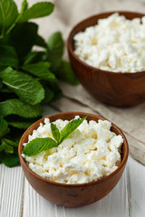 fresh homemade cottage cheese in a wood bowl with mint leaves, on white background. top view