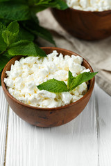 fresh homemade cottage cheese in a wood bowl with mint leaves, on white background. top view