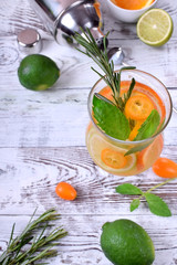 Sparkling beverage with slices of lime, kumquat and orange topped with mint against the white wooden background