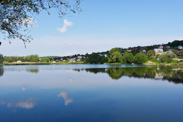 A lonely little cloud is reflected in a picturesque lake. Beautiful clean lake among the village.