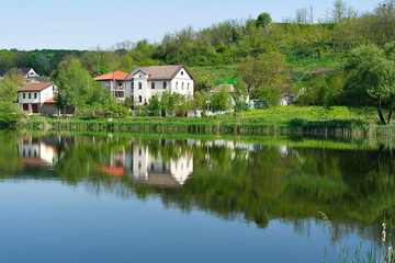Fototapeta na wymiar House under the hill on the lake. Clear summer day. Luxurious reflection in the lake.