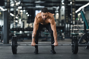 Fototapeta na wymiar Muscular bodybuilder lifting heavy barbell at gym interior