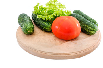 tomatoes, cucumbers and green salad on a wooden board on a white background