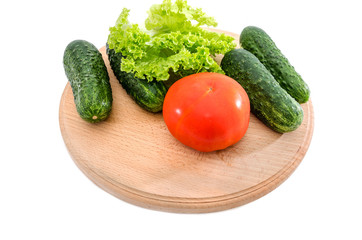 tomatoes, cucumbers and green salad on a wooden board on a white background
