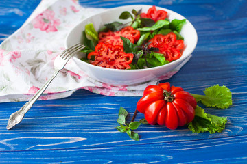 Salad with large ripe red tomato with basil on a blue wooden table, tomato variety.