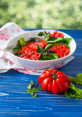 Salad with large ripe red tomato with basil on a blue wooden table, tomato variety.