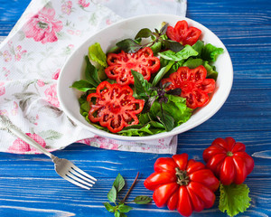 Salad with large ripe red tomato with basil on a blue wooden table, tomato variety.