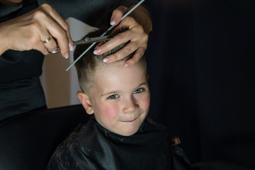 Happy little boy getting new hairstyle at barber shop