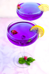 Thai asian purple Anchan tea in cocktail glasses with dry rosebuds, blue tea, tea and green basil leaves and slice of lemon, healthy organic detox Asian herbal tea clitoria Butterfly Pea on marble 