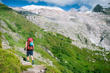Naklejka na ściany i meble A hiker walking along a steep path in the mountais towards a glacier and high peaks.
