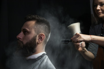 Professional hairdresser barber using talcum powder for his client hair sitting in a barber chair on black background