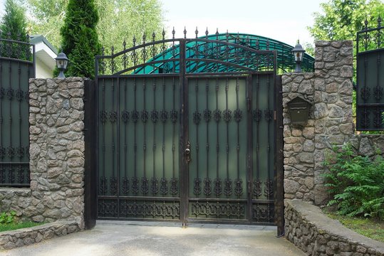 gray metal gates with black leather pattern and a stone fence in the street