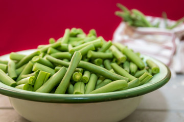 Fresh organic green beans in an antique enamel bowl on a red background