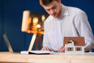 3d model of house on the table with male designer, architect working on the laptop on the background.