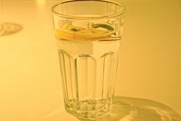 one clear glass full of drink and a piece of lemon on a yellow table