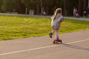 Little girl in a sunny park riding a scooter. Sunny spring afternoon sports activities