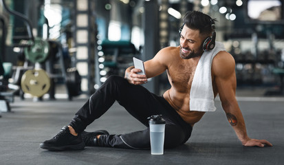 Fototapeta na wymiar Muscular man using cellphone at gym, free space