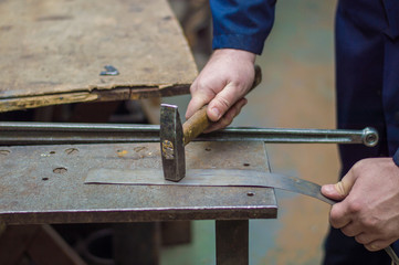 Professional locksmith in blue uniform working with hammer and steel at crafting table - metalworking industry concept. 
