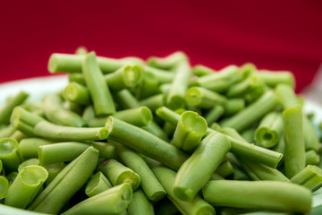 Fresh organic green beans in an antique enamel bowl on a red background