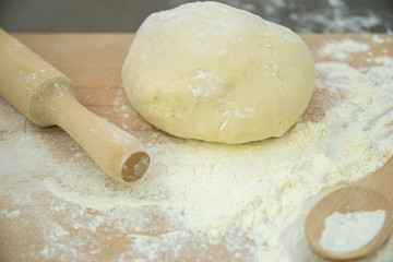 The prepared dough for pasta or dumplings lies on a wooden board sprinkled with flour , a rolling pin and a wooden spoon.  the cooking process