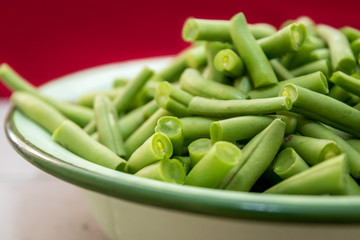 Fresh organic green beans in an antique enamel bowl on a red background