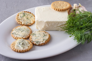Crackers with smeared garlic butter with dill on a white plate,