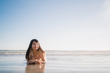 Obraz premium Young Asian woman feeling happy on beach, beautiful female happy relax smiling fun on beach near sea when sunset in evening. Lifestyle women travel on beach concept.