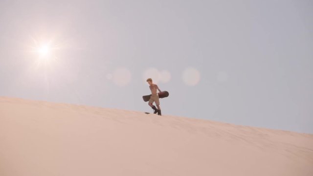 Sexy sportsman walking over the edge of the dunes of the atacama desert holding a sandboard. Xtrem sport sandboard.