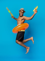 Playful black man jumping with water guns