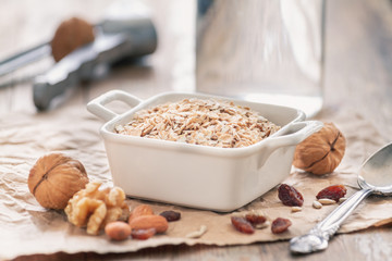 Oatmeal with walnuts, raisins and almonds in a white ceramic bowl on a vintage rustic wood background. Healthy nutrition breakfast concept.