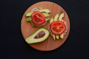 snack with avocado and tomato and half an avocado on wooden board