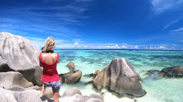 Back side of woman photographer with camera at Anse Source d'Argent, La Digue, Seychelles. Shallow waters, white pristine sand and turquoise sea. Summer holiday tropical travel. Horizont background.