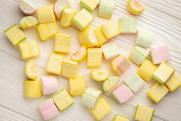 Multi-colored marshmallow chaotically scattered on a white wooden background