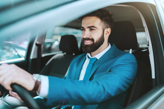 Young attractive prosperous Caucasian businessman in blue suit driving his car.